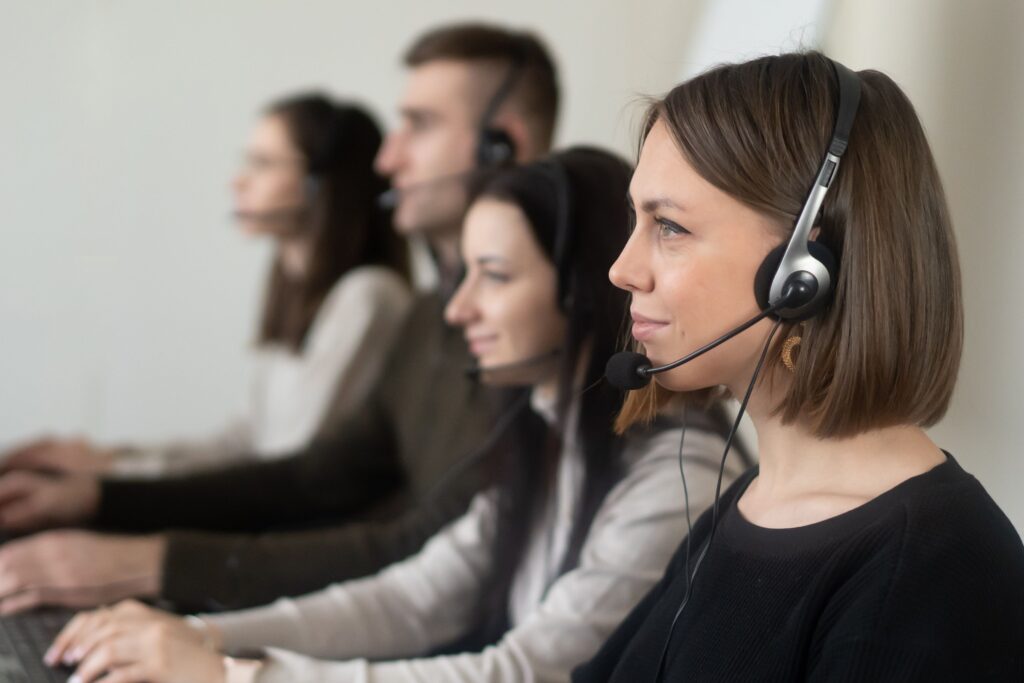 pexels photo 7035859 7035859 Side view of young coworkers in casual clothes sitting in light workplace with headphones with microphone while surfing on laptop